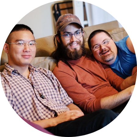 A photo of three members of L'Arche sitting on a couch together and smiling